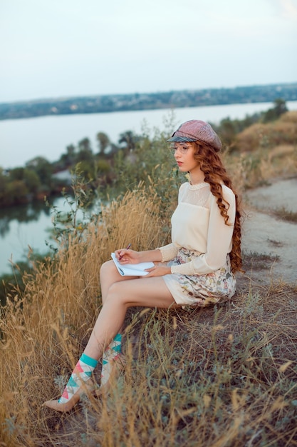 Estudiante pensando y escribiendo notas. Alegre niña feliz sentada escribiendo y leyendo al aire libre en la naturaleza.