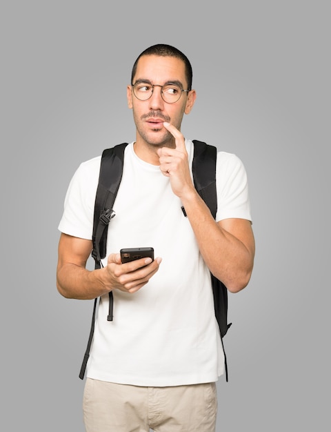 Estudiante pensativo usando su teléfono móvil