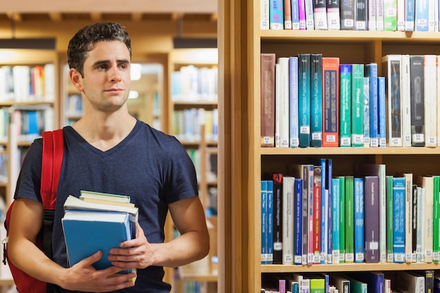 Estudiante de pie en la biblioteca con pila de libros