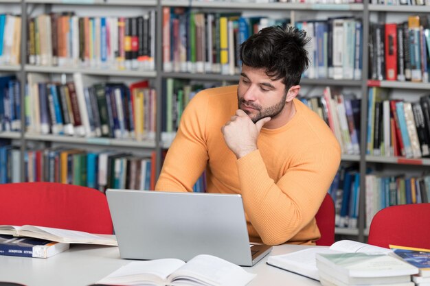 Estudiante preparando exámenes y lecciones de aprendizaje en la biblioteca escolar investigando en una computadora portátil y navegando por InternetxA en la biblioteca