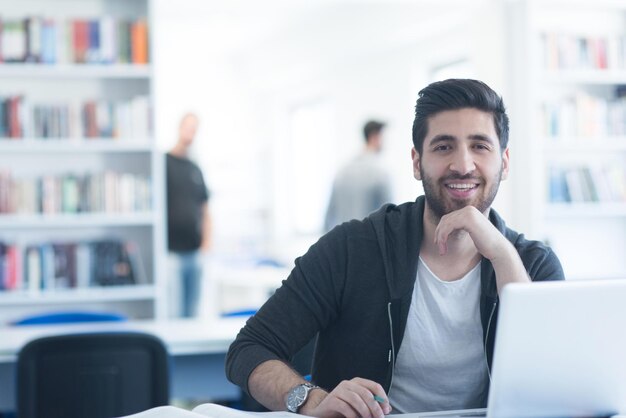 estudiante preparándose para un examen y aprendiendo lecciones en la biblioteca de la escuela haciendo investigación en una computadora portátil y navegando por Internet