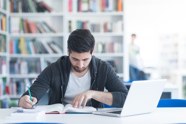 estudiante preparándose para un examen y aprendiendo lecciones en la biblioteca de la escuela haciendo investigación en una computadora portátil y navegando por Internet