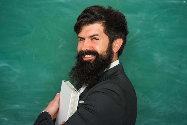 Estudiante preparándose para la prueba o el examen del día del maestro joven maestro barbudo cerca de la pizarra en la escuela clas