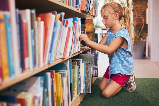 Foto estudiante que busca un libro para leer en la biblioteca escolar estudiante que selecciona literatura para leer