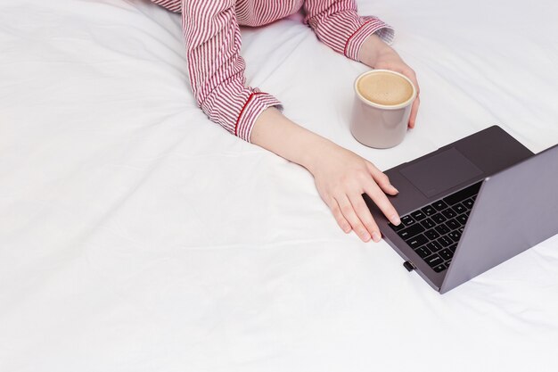 Estudiante que estudia de forma remota desde casa, está vestida con un pijama de rayas rosas y toma café.