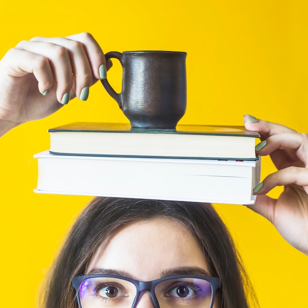 Foto una estudiante que lleva gafas sostiene una pila de libros y una taza de café.