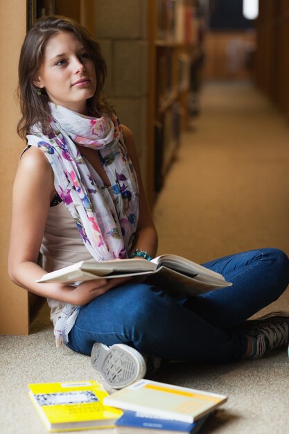 Estudiante reflexivo sentado con libros en la biblioteca