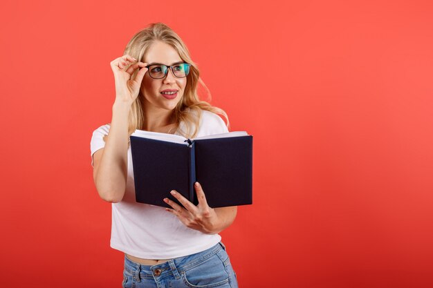 Estudiante rubia que sonríe corrigiendo los vidrios que sostienen el libro de texto.