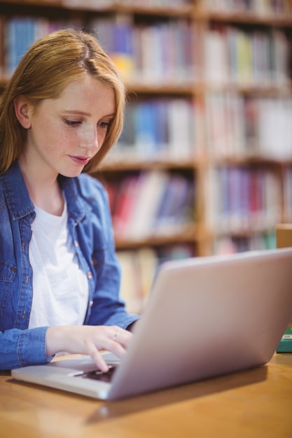 Estudiante rubia que usa la computadora portátil en biblioteca