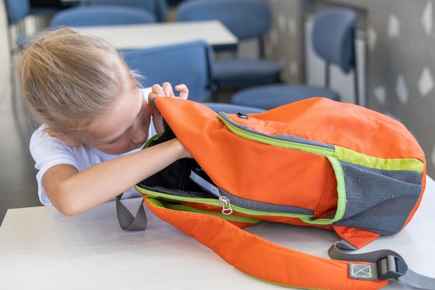 El estudiante saca libros de papelería de una mochila Una niña mira dentro de una mochila escolar Regreso a la escuela