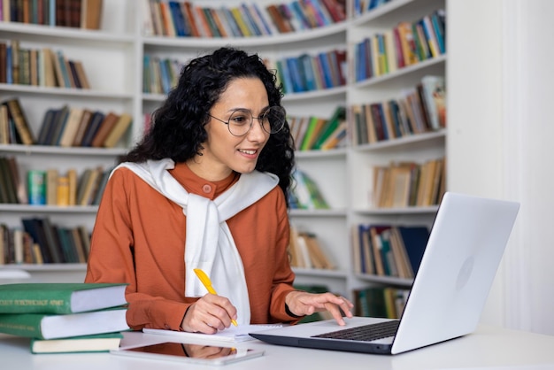Una estudiante satisfecha escucha una conferencia en línea en una computadora portátil escribe algo en un cuaderno