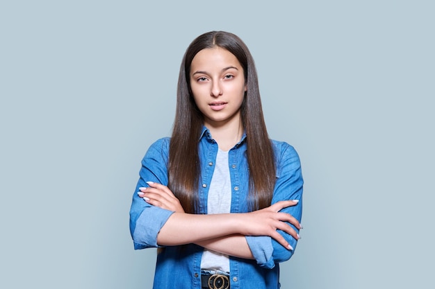 Estudiante de secundaria adolescente confiada mirando la cámara sobre fondo de estudio de color gris brillante Mujer atractiva posando con los brazos cruzados Concepto de educación de estudio de adolescencia