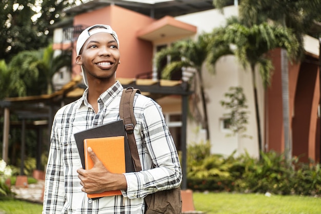 Estudiante seguro con una gorra y sosteniendo libros