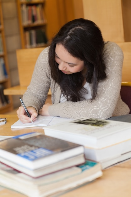 Estudiante sentado en una biblioteca en un escritorio y escribiendo