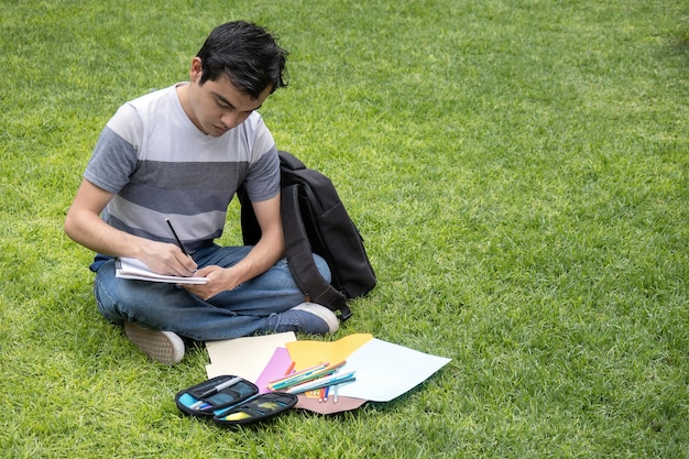 Un estudiante sentado en el césped de la escuela escribiendo en un bloc de notas con espacio para el texto