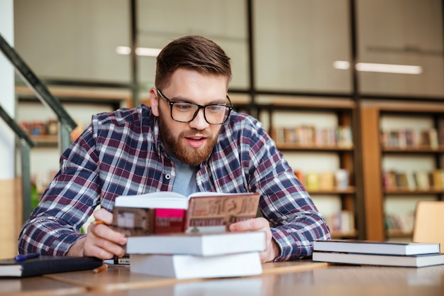 Estudiante sentado en el escritorio y leyendo un libro en la biblioteca