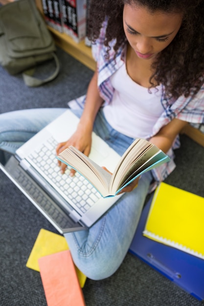 Foto estudiante sentado en el piso en la biblioteca usando la computadora portátil