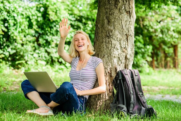 Una estudiante se sienta en el césped mientras estudia la naturaleza, el bienestar esencial y la capacidad de ser productiva.