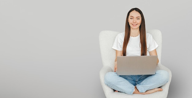 Estudiante se sienta en una silla con una computadora portátil sonriendo y mirando a la cámara