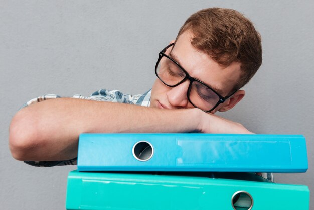 Estudiante soñoliento en vasos con carpetas. durmiendo en carpetas aisladas en gris
