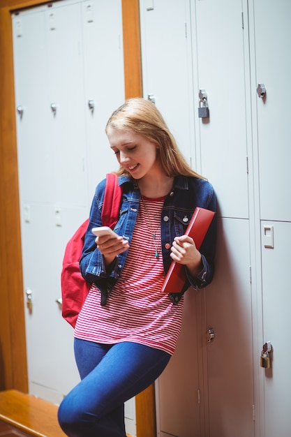 Estudiante sonriente apoyado contra el armario con smartphone