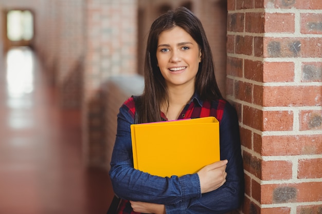 Estudiante sonriente con carpeta posando en el pasillo