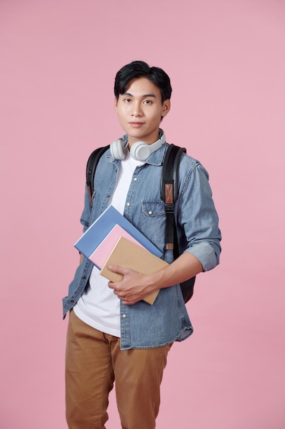 Estudiante sonriente feliz de pie con mochila y carpetas sobre fondo de color rosa