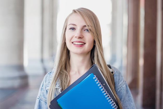 Estudiante sonriente feliz tiene un cuaderno azul en sus manos