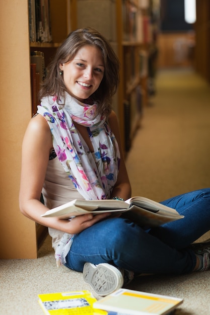 Estudiante sonriente con libros en el pasillo de la biblioteca