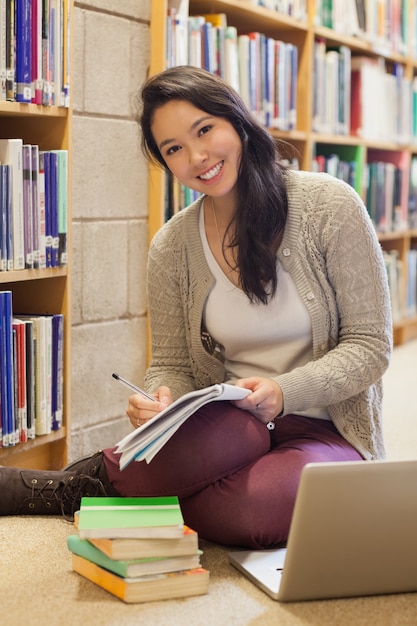 Estudiante sonriente que trabaja en el piso de la biblioteca