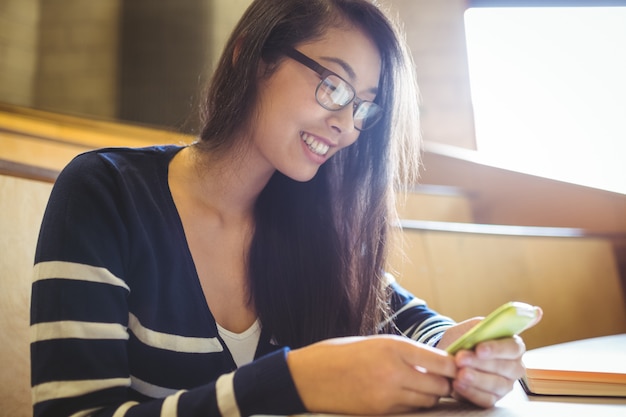 Estudiante sonriente que usa el teléfono inteligente en la universidad