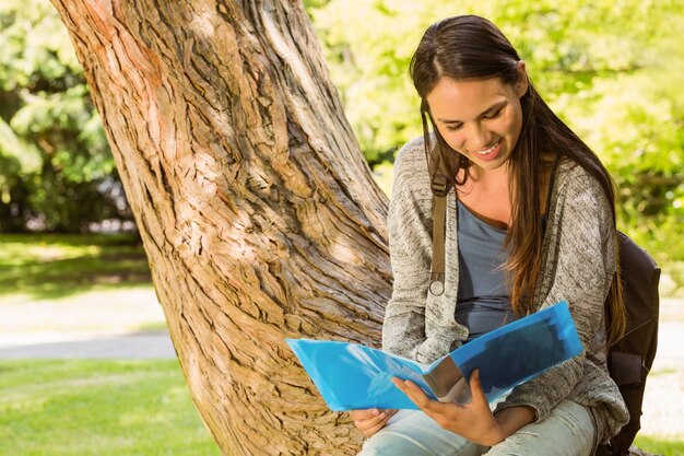 Estudiante sonriente sentado en el tronco y libro de lectura