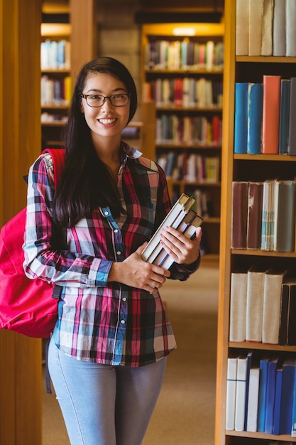 Foto estudiante sonriente sosteniendo libros en la biblioteca