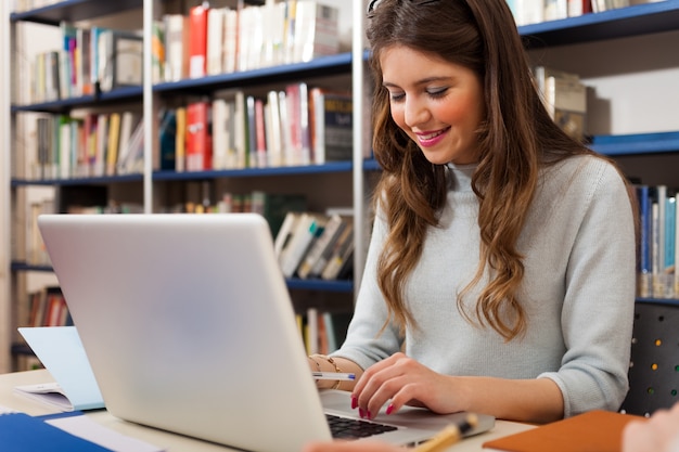 Estudiante sonriente usando su computadora portátil en una biblioteca