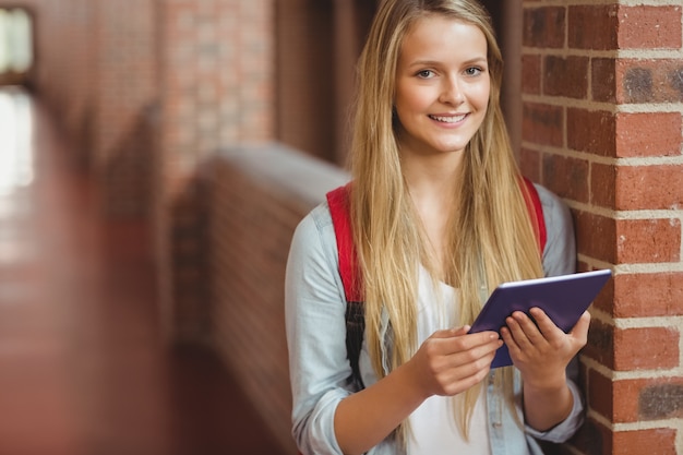 Estudiante sonriente usando tableta en el pasillo de la universidad