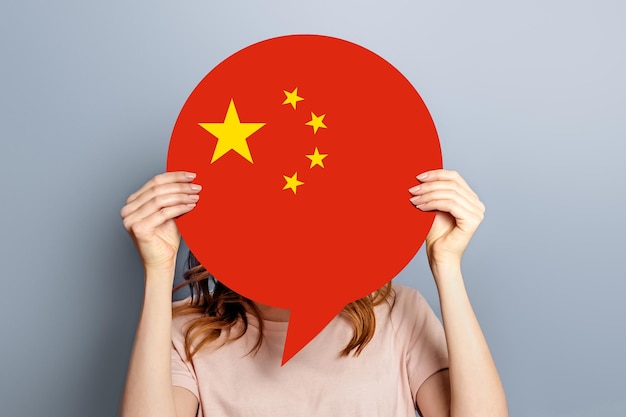 Una estudiante sostiene una burbuja de voz en blanco con una bandera china aislada sobre un fondo gris de estudio