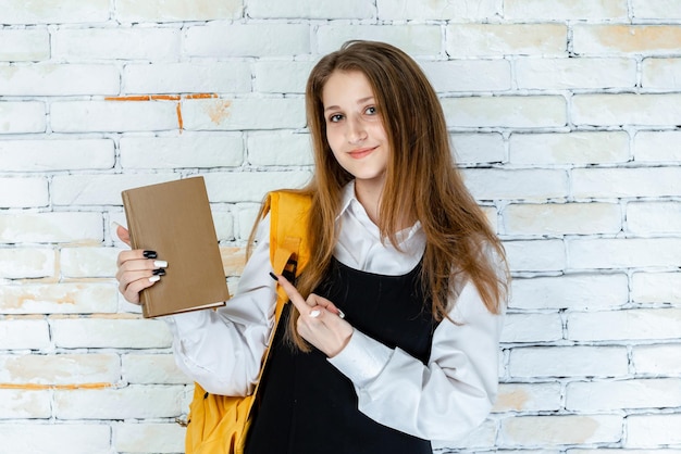 Estudiante en uniforme sosteniendo un libro y señalándolo con el dedo Foto de alta calidad