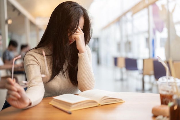 Una estudiante universitaria asiática cansada e infeliz que sufre de fatiga ocular se quita las gafas.