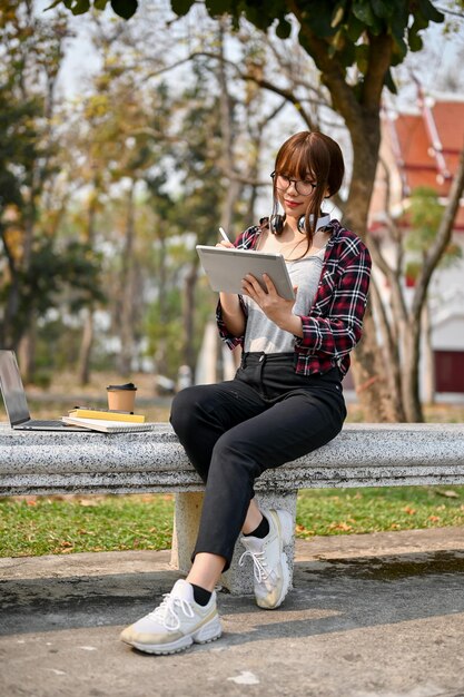 Estudiante universitaria asiática se sienta en un banco y usa su tableta digital portátil