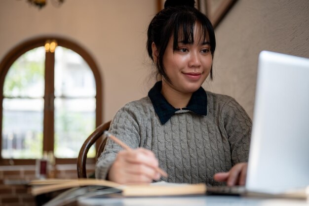 Una estudiante universitaria se centra en su trabajo en su computadora portátil trabajando remotamente en una cafetería