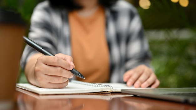 Una estudiante universitaria escribiendo y tomando notas en su cuaderno en un café al aire libre