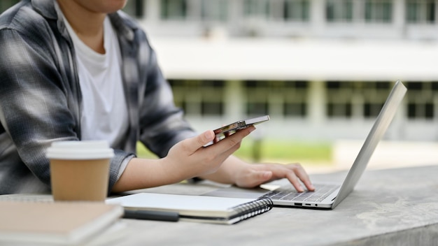 Una estudiante universitaria que usa su teléfono inteligente y su computadora portátil en un parque del campus