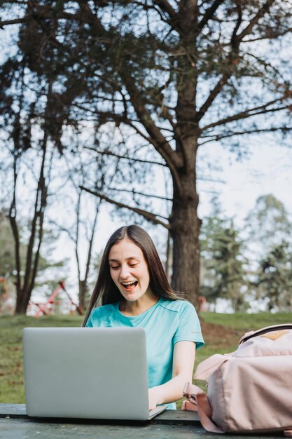 Foto estudiante universitaria riendo y usando su laptop en el parque del campus universitario. camiseta turquesa