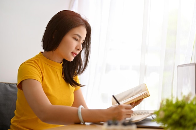 Estudiante universitaria se sienta en la biblioteca tomando notas en su cuaderno escolar