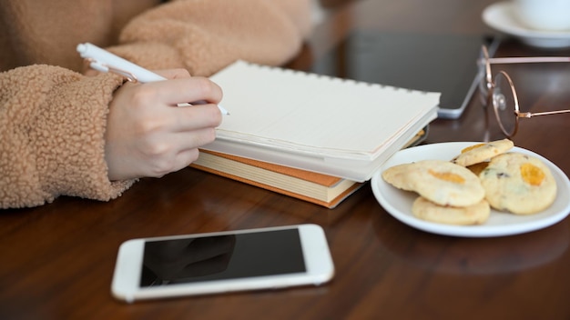 Estudiante universitaria tomando notas en su bloc de notas en espiral mientras come galletas en la cafetería