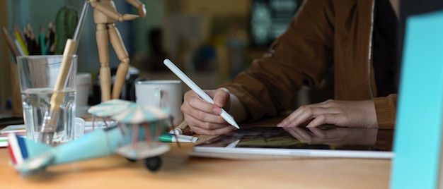 Estudiante universitario femenino haciendo tarea con tableta digital, libros y suministros en mesa de madera