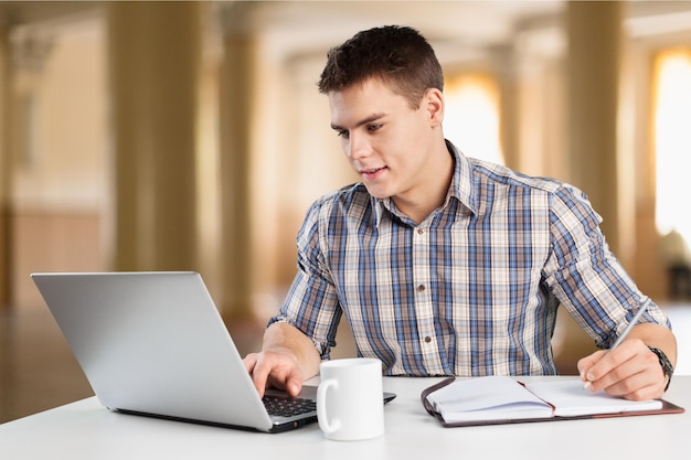Estudiante universitario guapo usando su computadora portátil en el campus