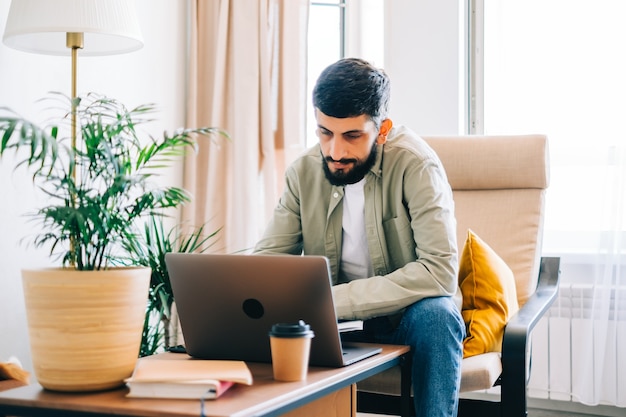 Estudiante universitario de hombre caucásico, estudiando con la computadora portátil a distancia preparándose para el ensayo de escritura de examen de prueba haciendo la tarea en casa, concepto de educación a distancia.