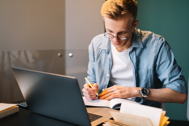 Estudiante universitario hombre caucásico en gafas que estudian con la computadora portátil a distancia preparándose para el examen de prueba escribiendo un ensayo haciendo la tarea en casa