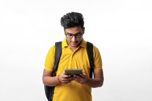 Estudiante universitario indio joven que usa la tableta sobre el fondo blanco.